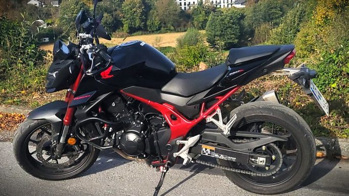 Schwarzes Motorrad mit roten Akzenten in einer ländlichen Umgebung.