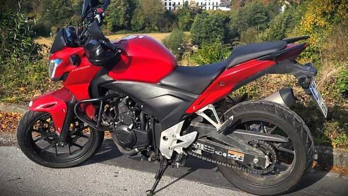 Rotes Motorrad auf einer Straße, umgeben von Bäumen und grünem Gelände.