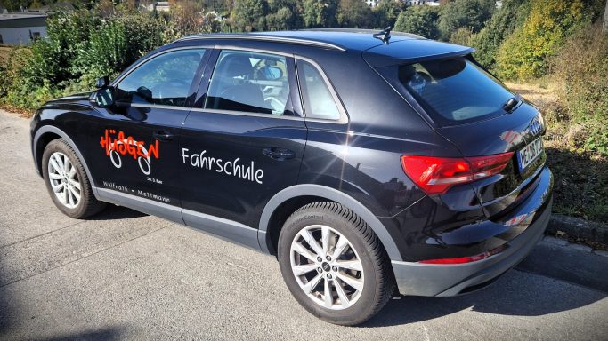 Schwarzes SUV mit Logo und Schriftzug auf der Seite, parkt in einer grünen Umgebung.