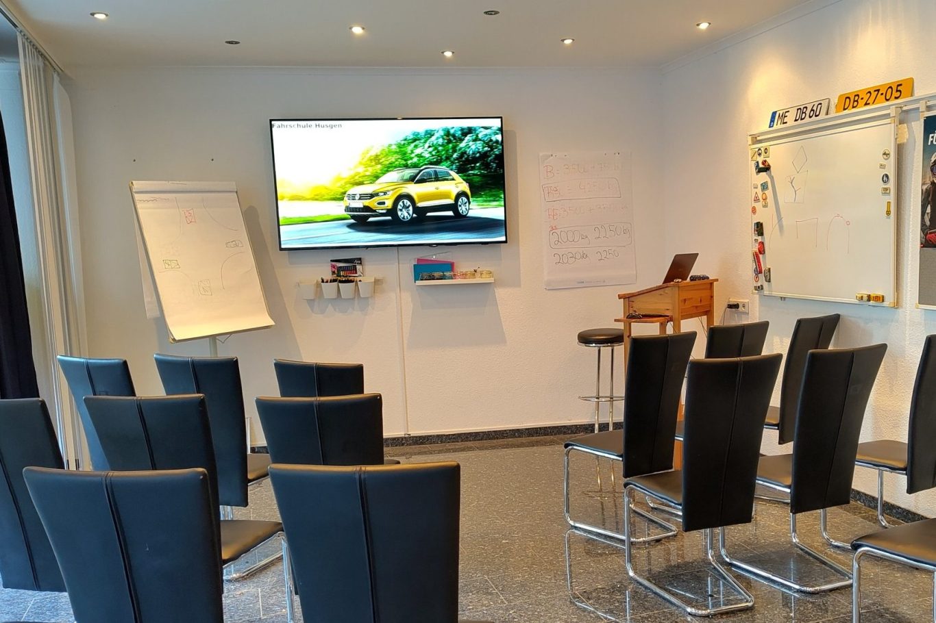 Besprechungsraum mit Stühlen, Whiteboard und einem Bildschirm, der ein Auto zeigt.