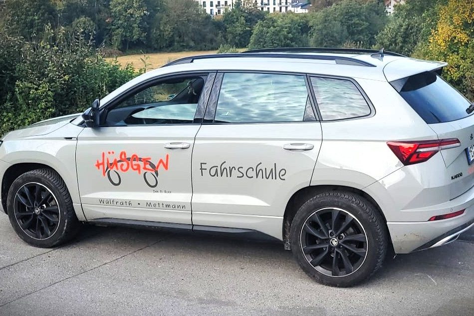 Grauer SUV mit Aufschrift „Fahrschule“ und dem Logo "Hüsgen" auf der Seitentür.