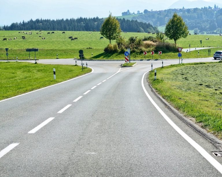 Kreuzung mit einer Rundfahrt umgeben von Wiesen und Bäumen im Hintergrund.